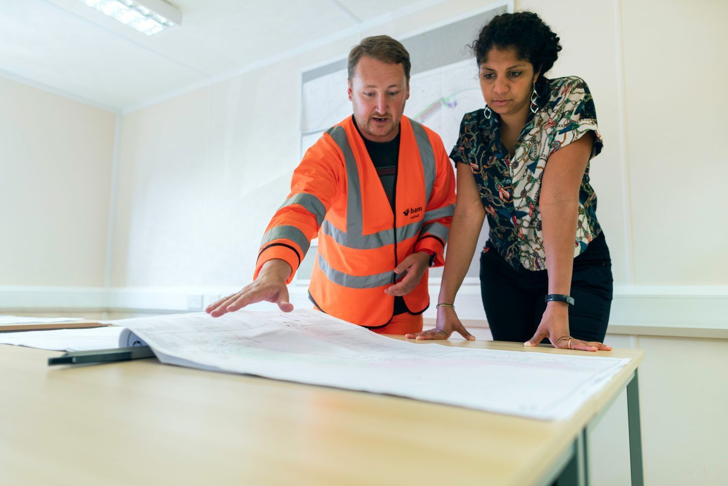 Two people reviewing a large floor plan on a table in a bright room