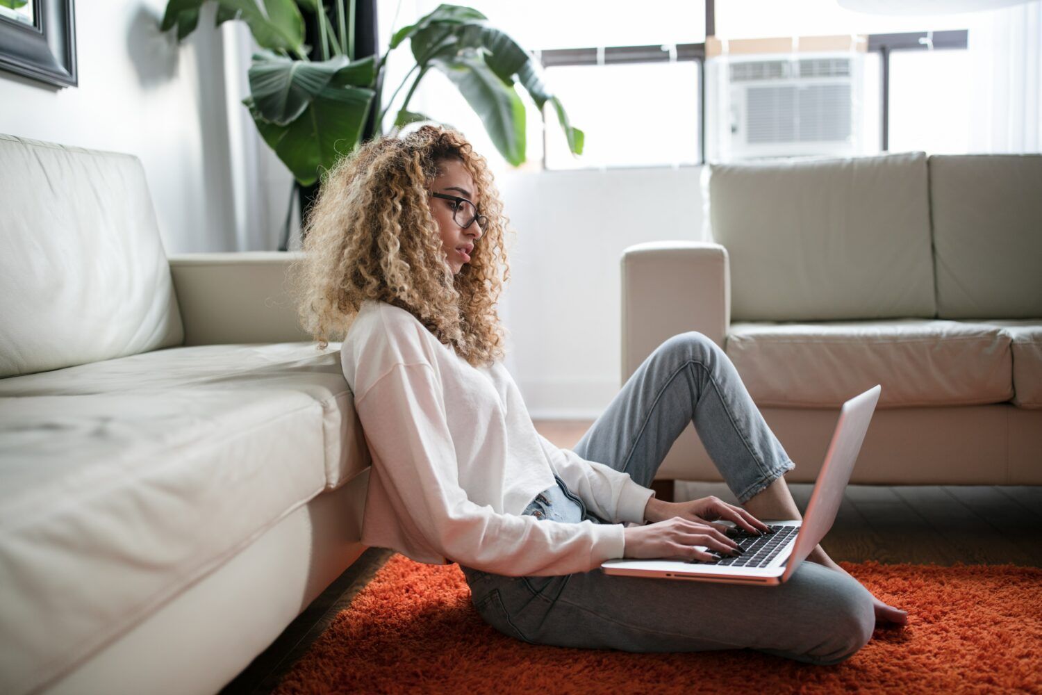 Person working on a laptop on an orange rug in a bright living room