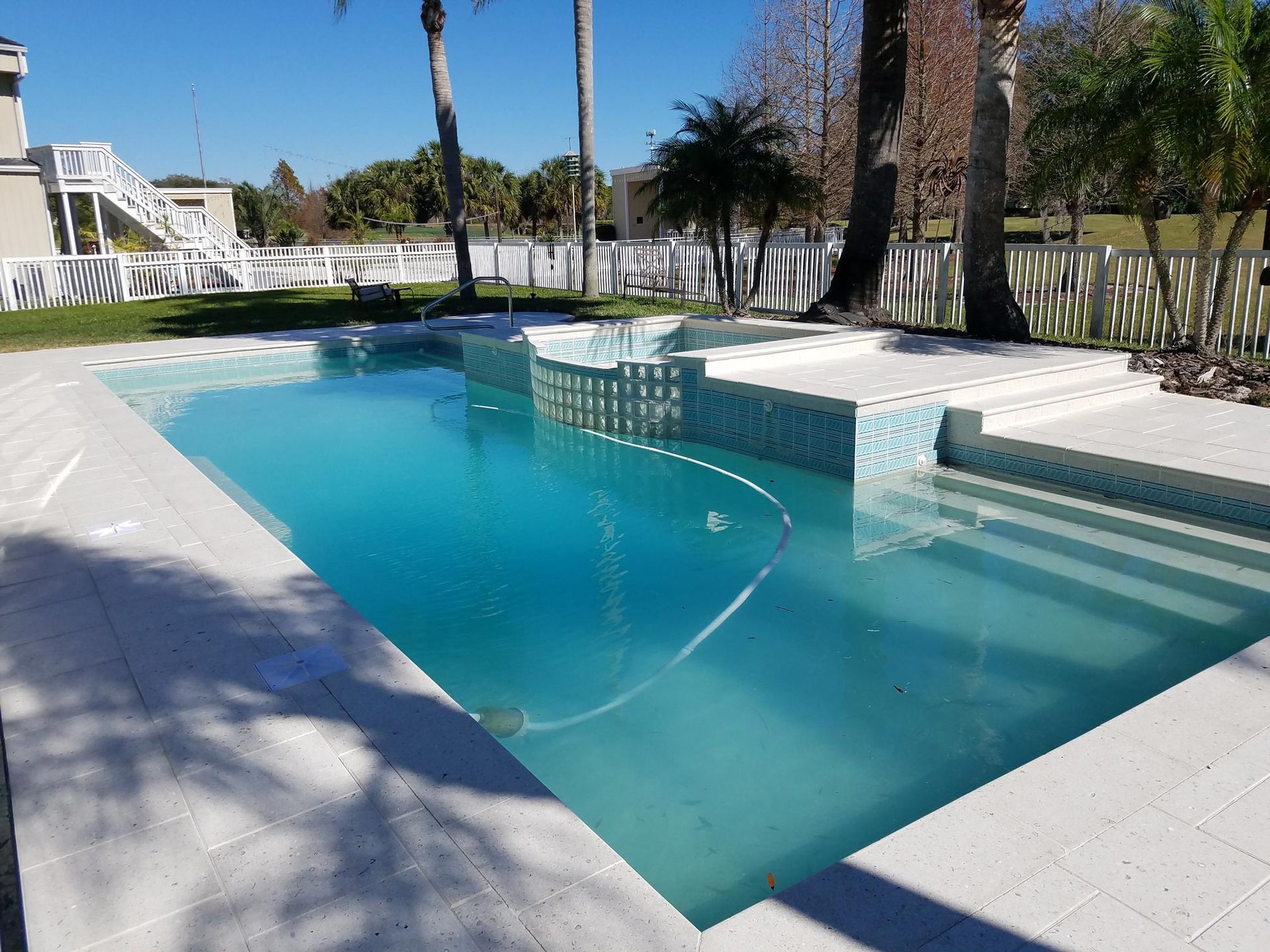 Sun Pavers open-air pool deck in Tampa, FL with turquoise pool, white concrete decking, and palm trees.