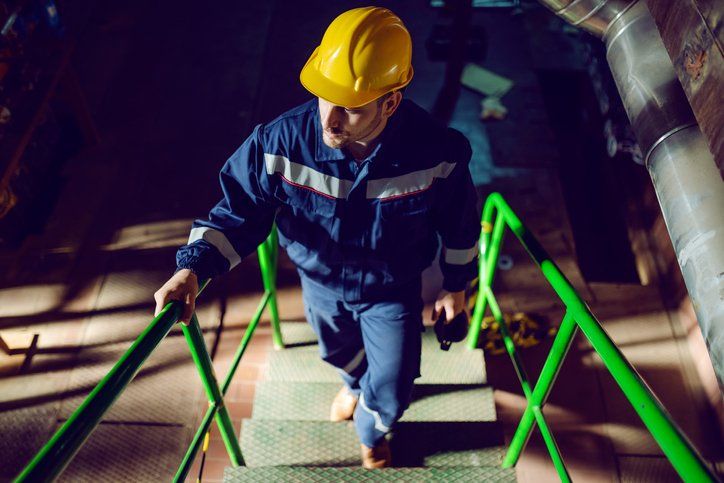 Worker dressed in blue work suit and with protective helmet on head climbing stairs