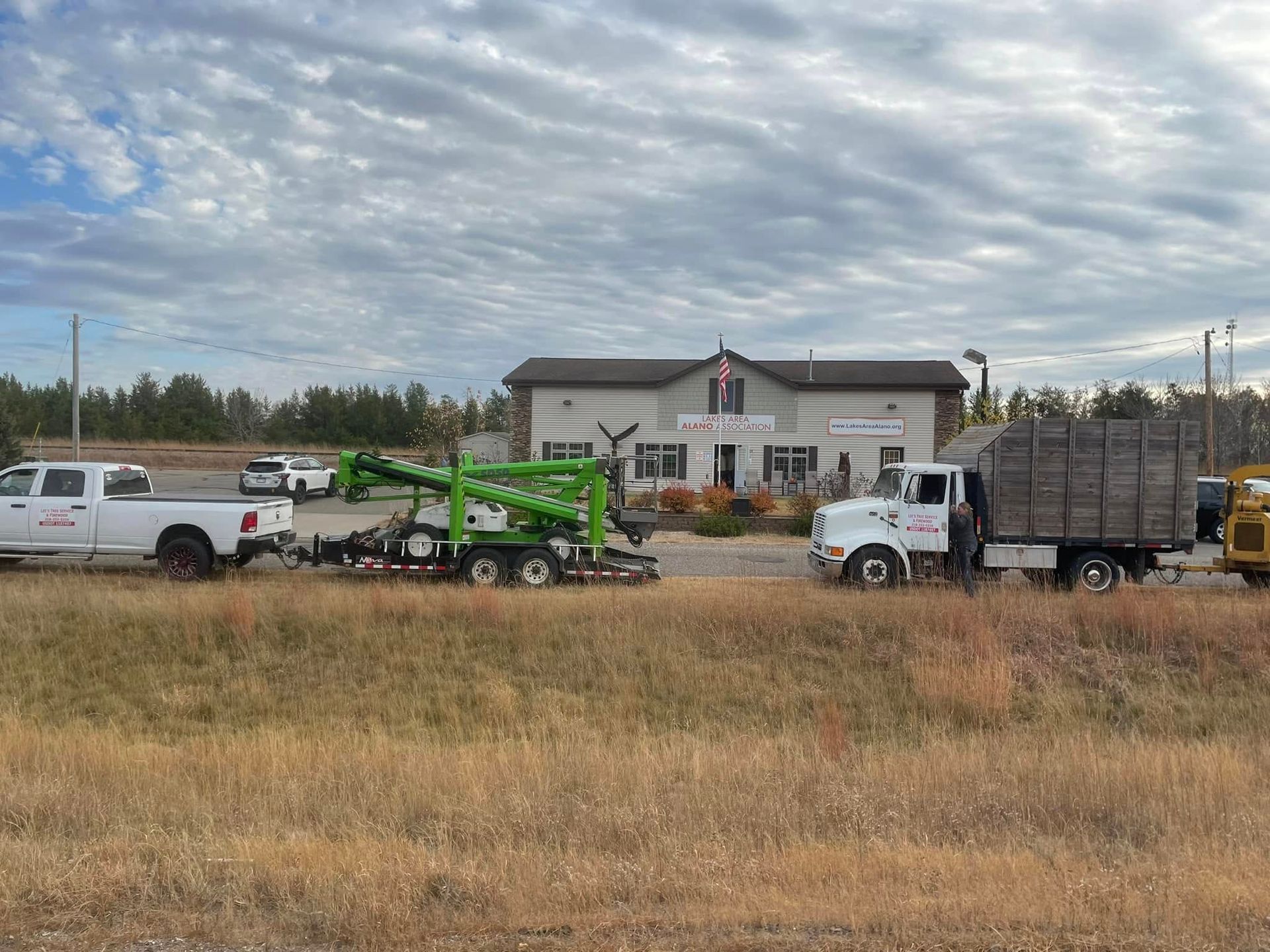 Two trucks are parked in a field in front of a building.