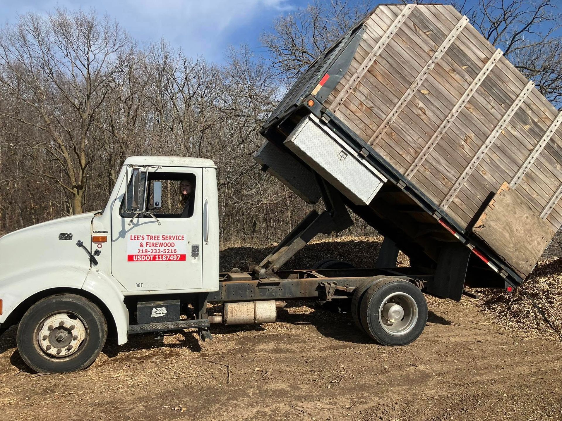 A white dump truck with a wooden bed is parked in a field.