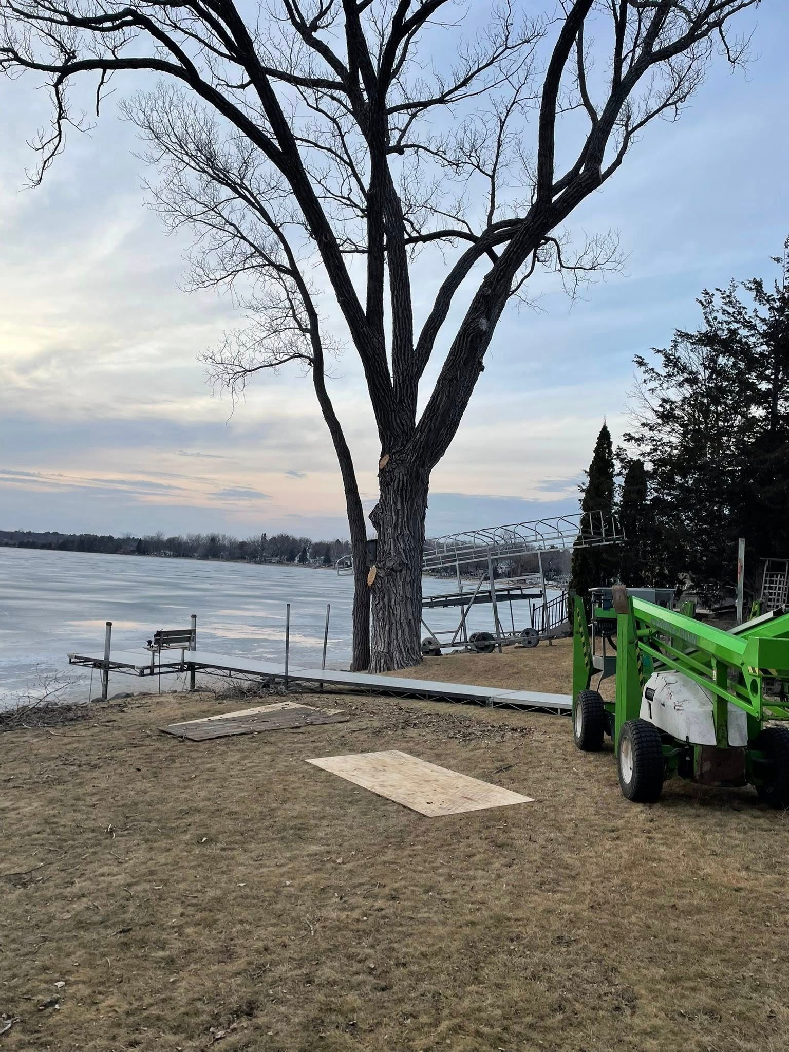 A green tractor is parked in front of a tree next to a body of water.