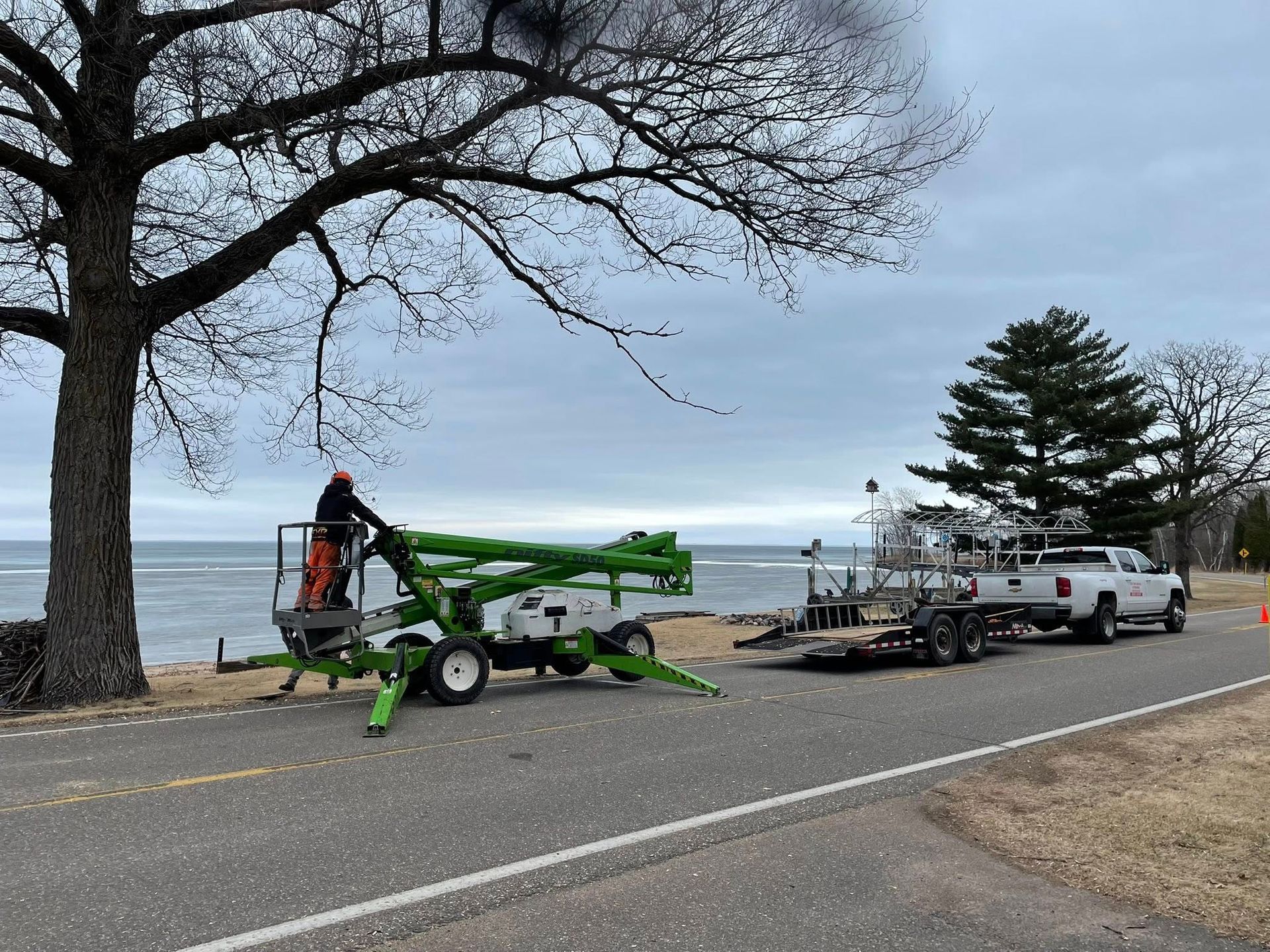 A man is standing on a lift next to a truck on the side of the road.