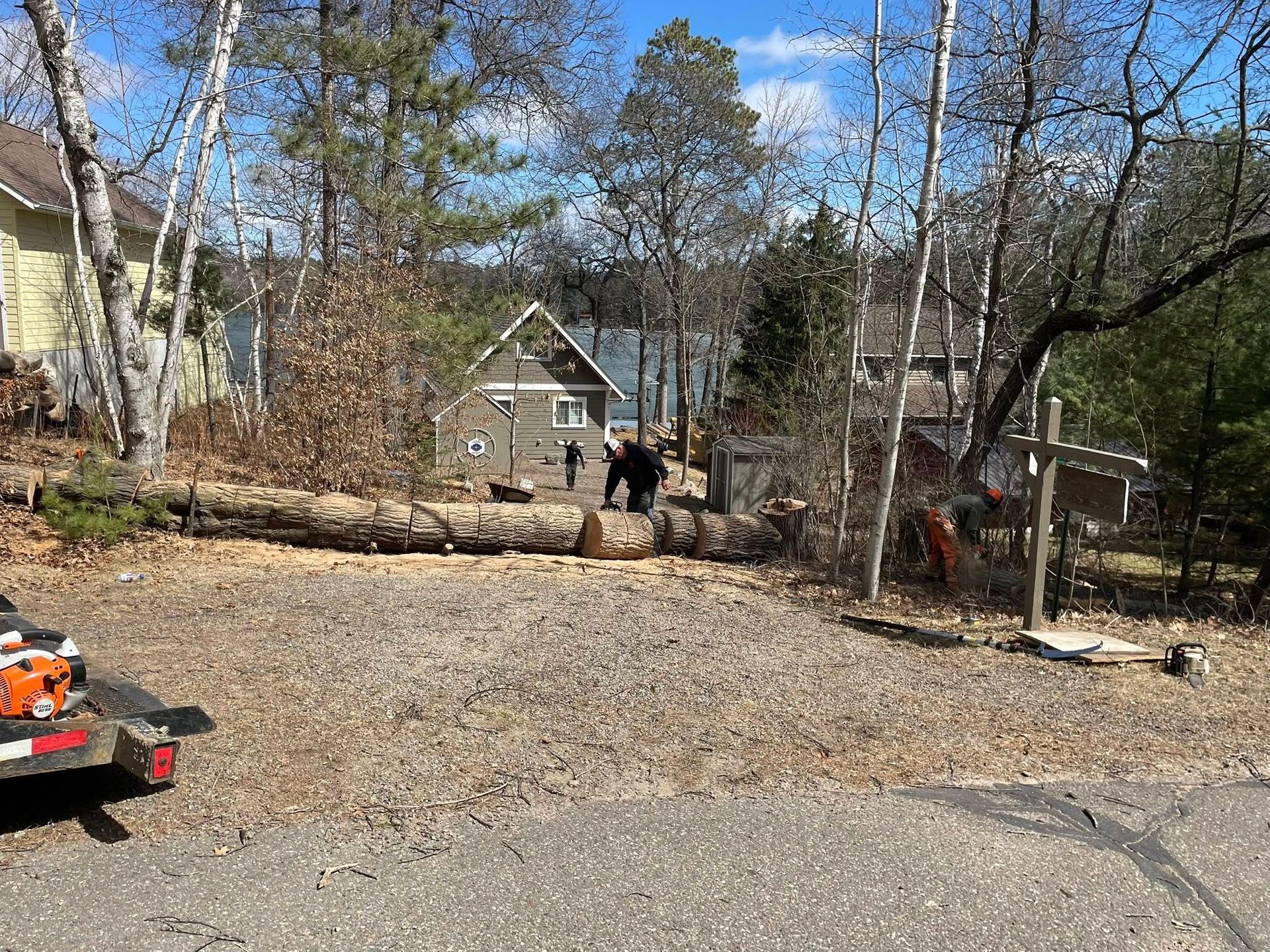 A man is cutting a large log with a chainsaw in a parking lot.