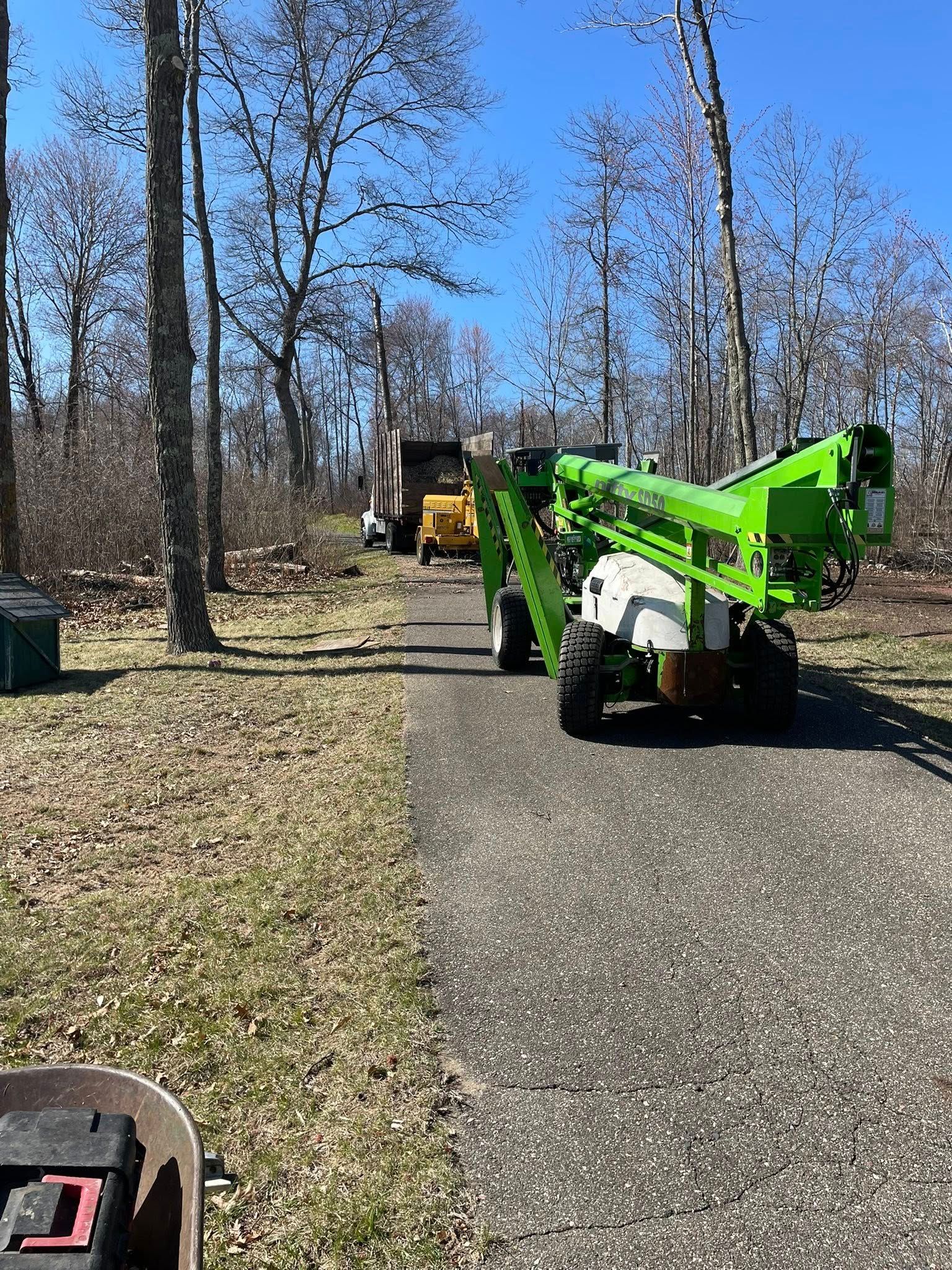 A green crane is parked on the side of a road next to a wheelbarrow.