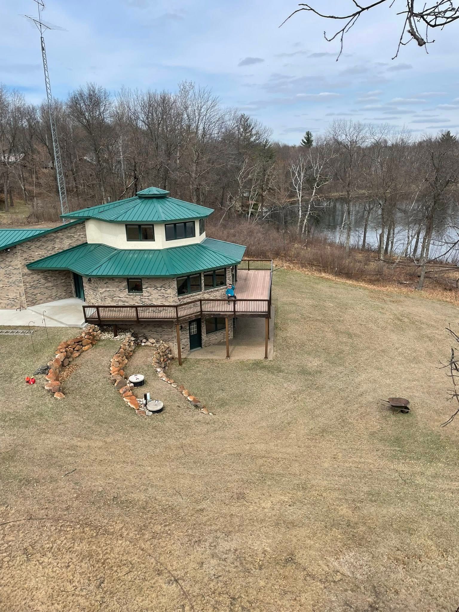 A large house with a green roof is sitting in the middle of a field next to a lake.