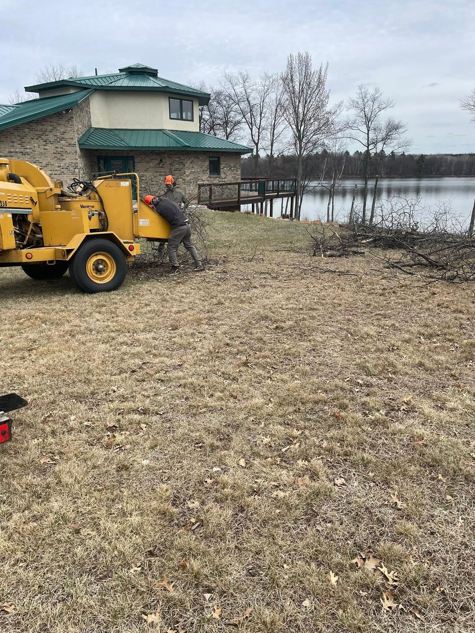A man is working on a tree stump grinder in a field in front of a house.