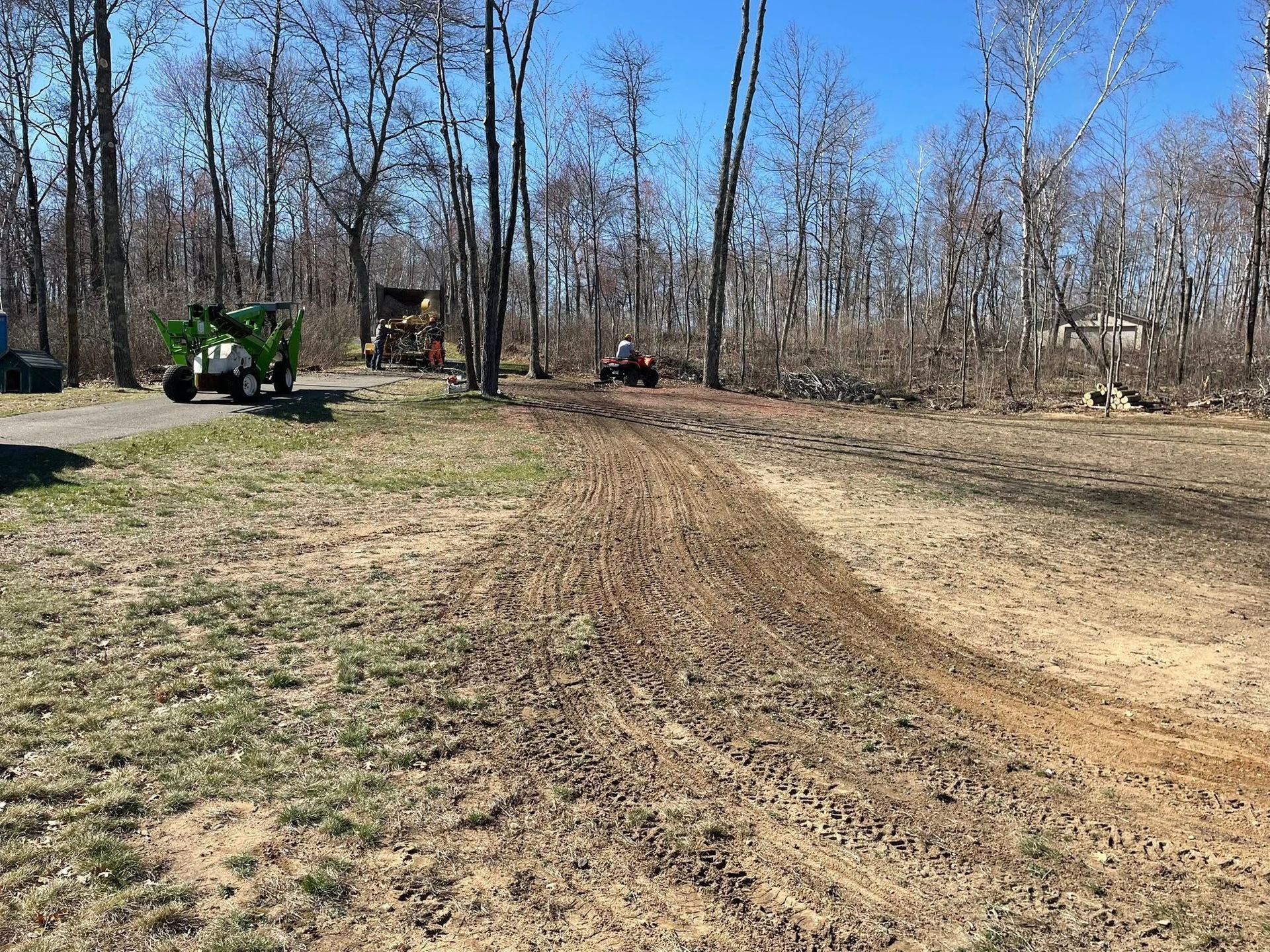 A green tractor is driving down a dirt road next to a forest.