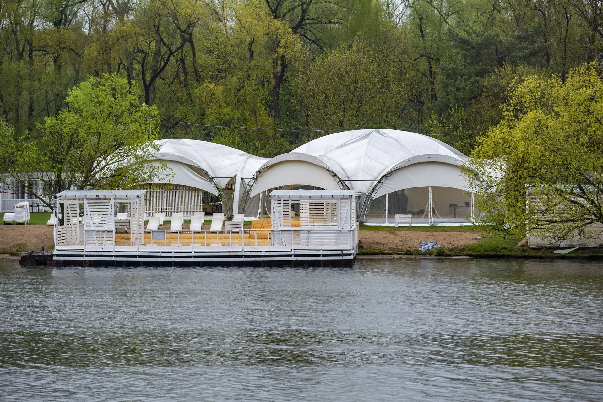 Tenda da sole beige che si estende su un balcone, accanto a un edificio con persiane marroni. Cielo azzurro sullo sfondo.
