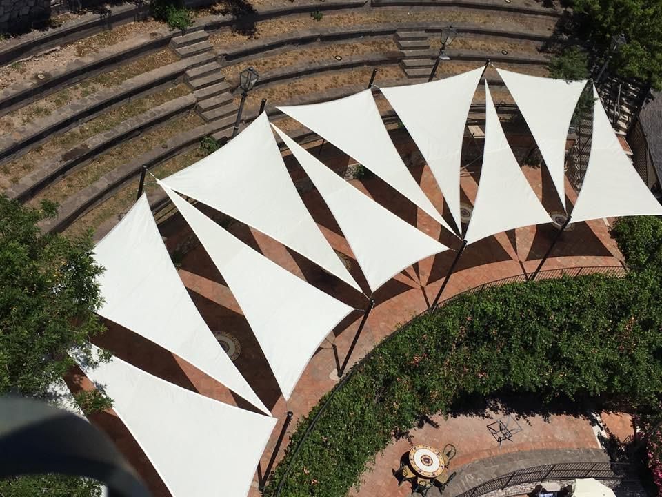 Gazebo con vista sulla piscina, tetto in tela beige, muro in pietra, piante, giornata di sole.