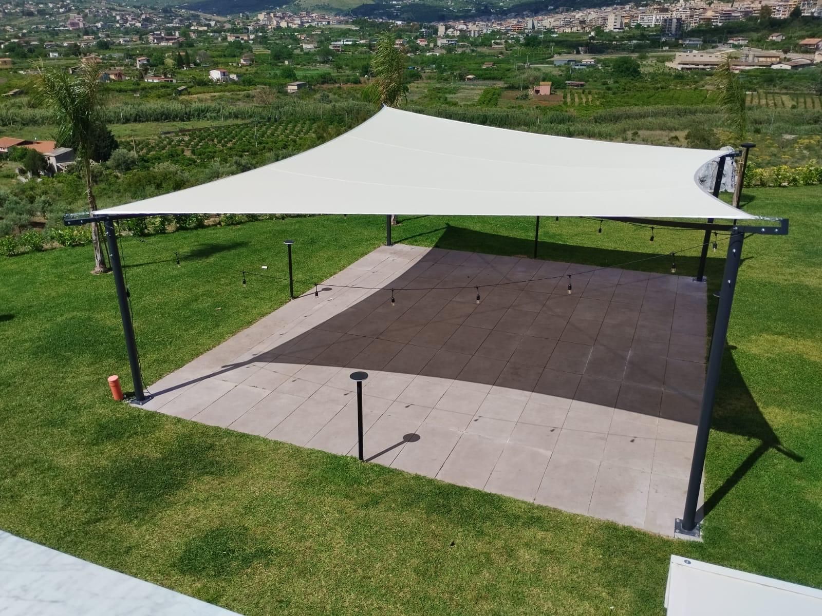 Tenda da sole beige che si estende su un balcone, accanto a un edificio con persiane marroni. Cielo azzurro sullo sfondo.