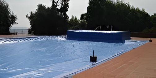 Una piscina coperta da un telo blu. Sullo sfondo si vedono alberi e uno specchio d'acqua in lontananza.