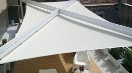 Vela ombreggiante triangolare bianca su un ponte, sostenuta da una struttura in metallo bianco.