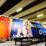 Un trailer con una pubblicità di Riviera Holidays. Una donna in costume da bagno sguazza in una piscina. Sito web e logo visibili.