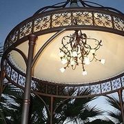Gazebo ornamentale con lampadario, struttura in metallo marrone, soffitto chiaro e palme sottostanti.