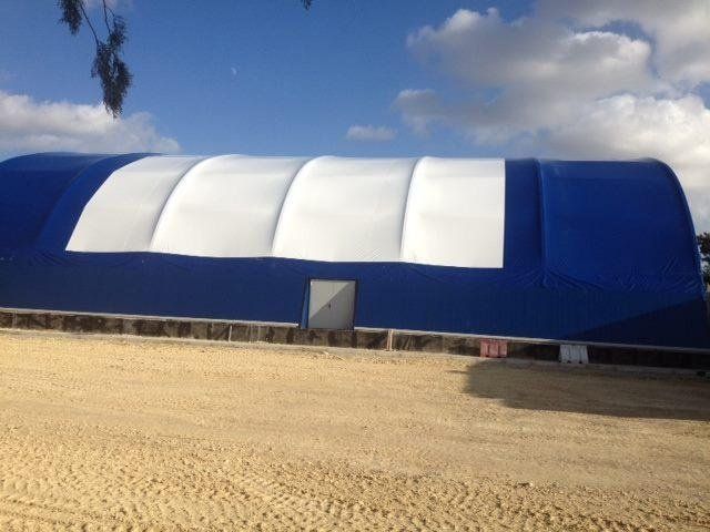Edificio in tessuto blu e bianco con una sola porta, situato su un terreno sabbioso, sotto un cielo azzurro nuvoloso.