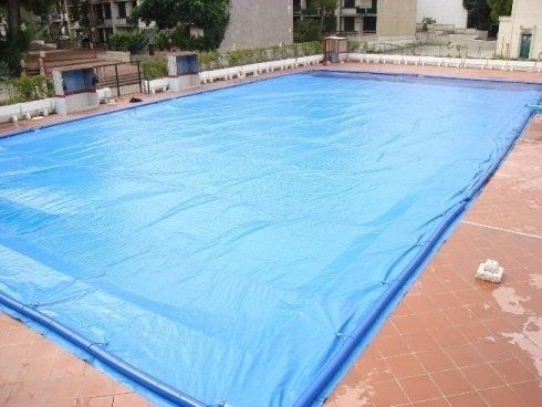 Copertura blu per piscina rettangolare su un patio in mattoni.