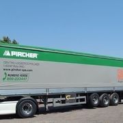 Autoarticolato Pircher verde e grigio con scritta, parcheggiato in una giornata di sole.