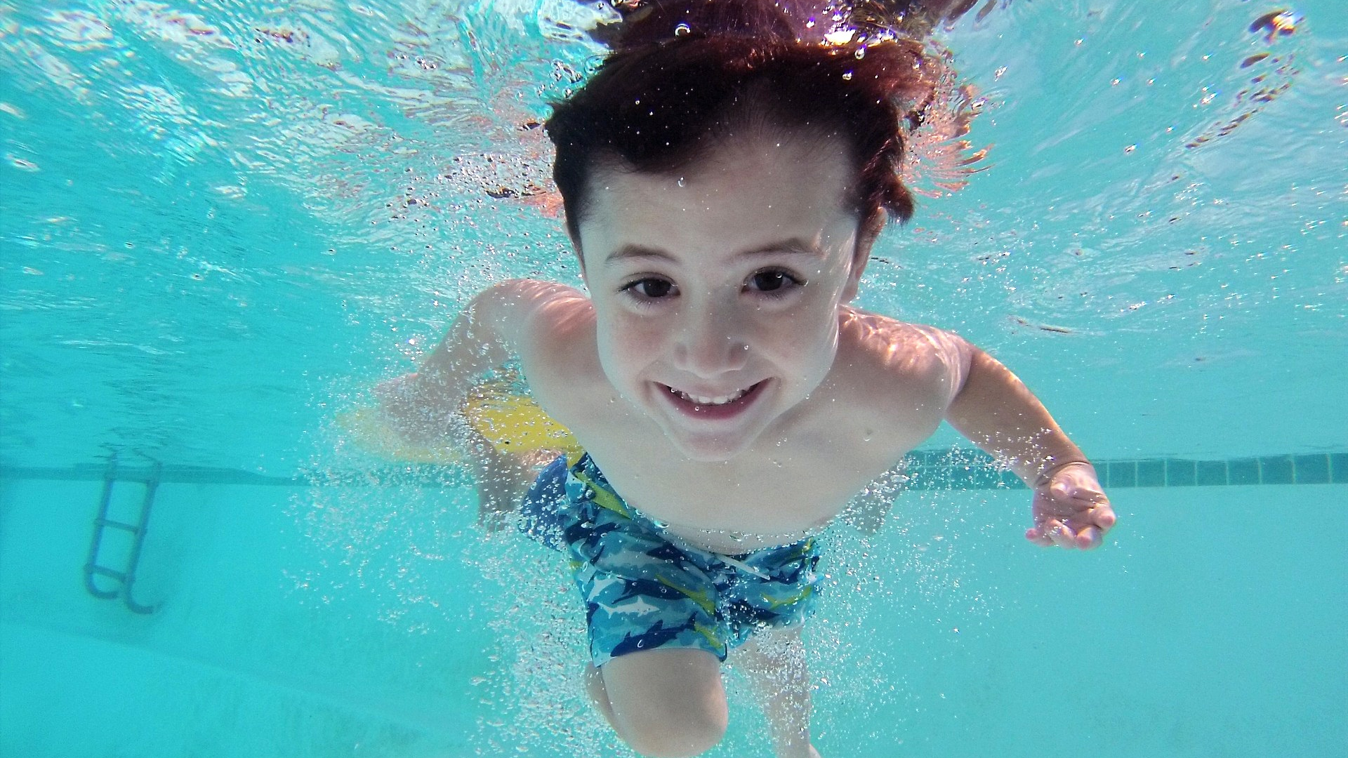 A young boy is swimming underwater in a swimming pool.