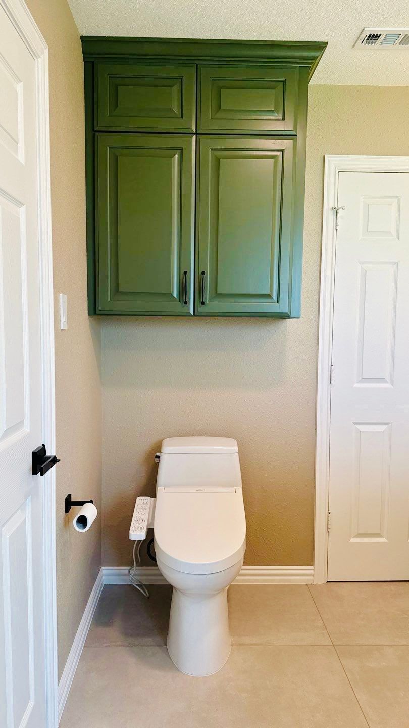 Green cabinet over a toilet in a bathroom with beige walls and a white door.