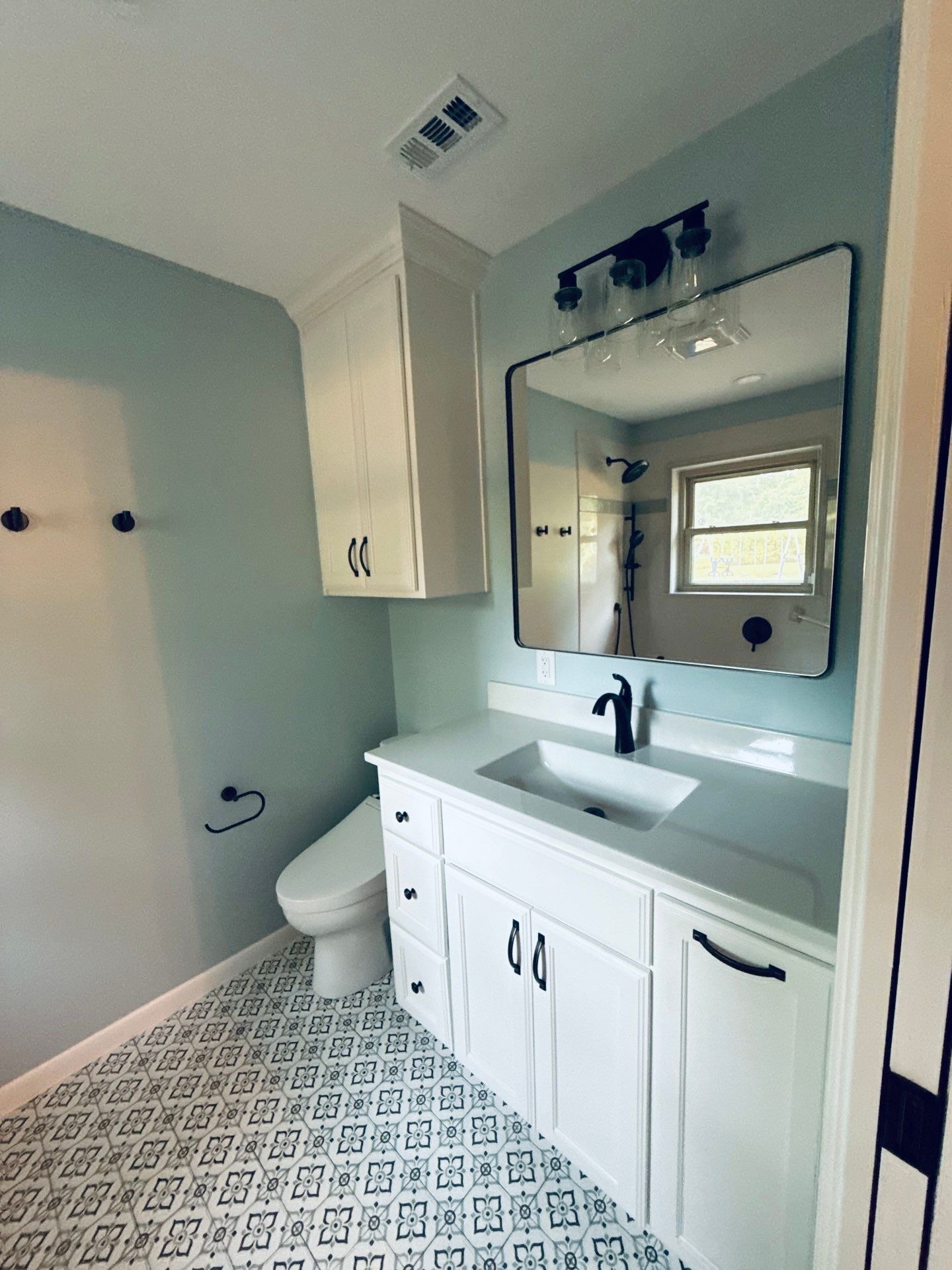 Bathroom with white vanity, pale blue walls, patterned tile floor, and a black-framed mirror.