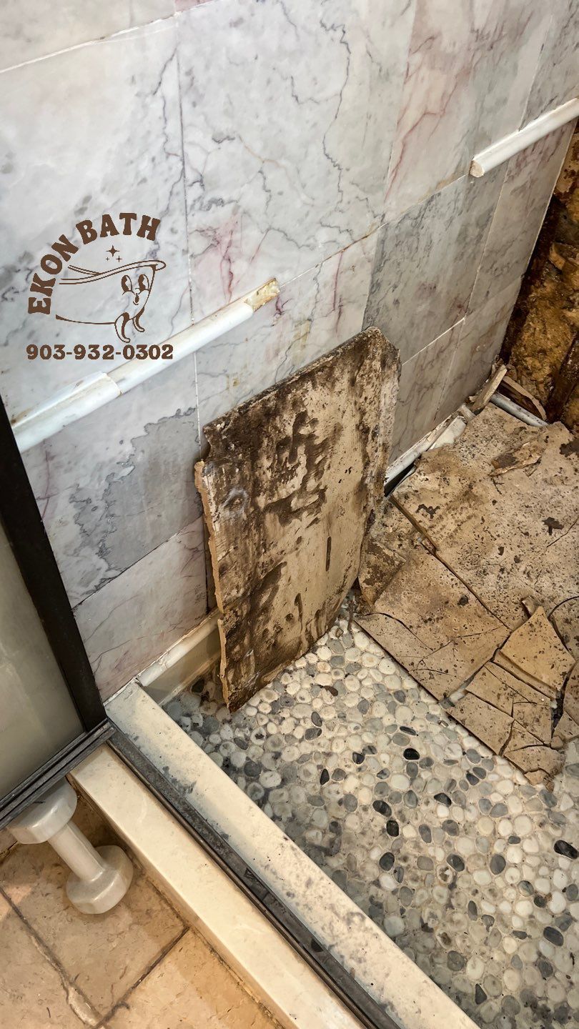 A shower stall with a tile floor and a marble wall with damaged and moldy wallboard.