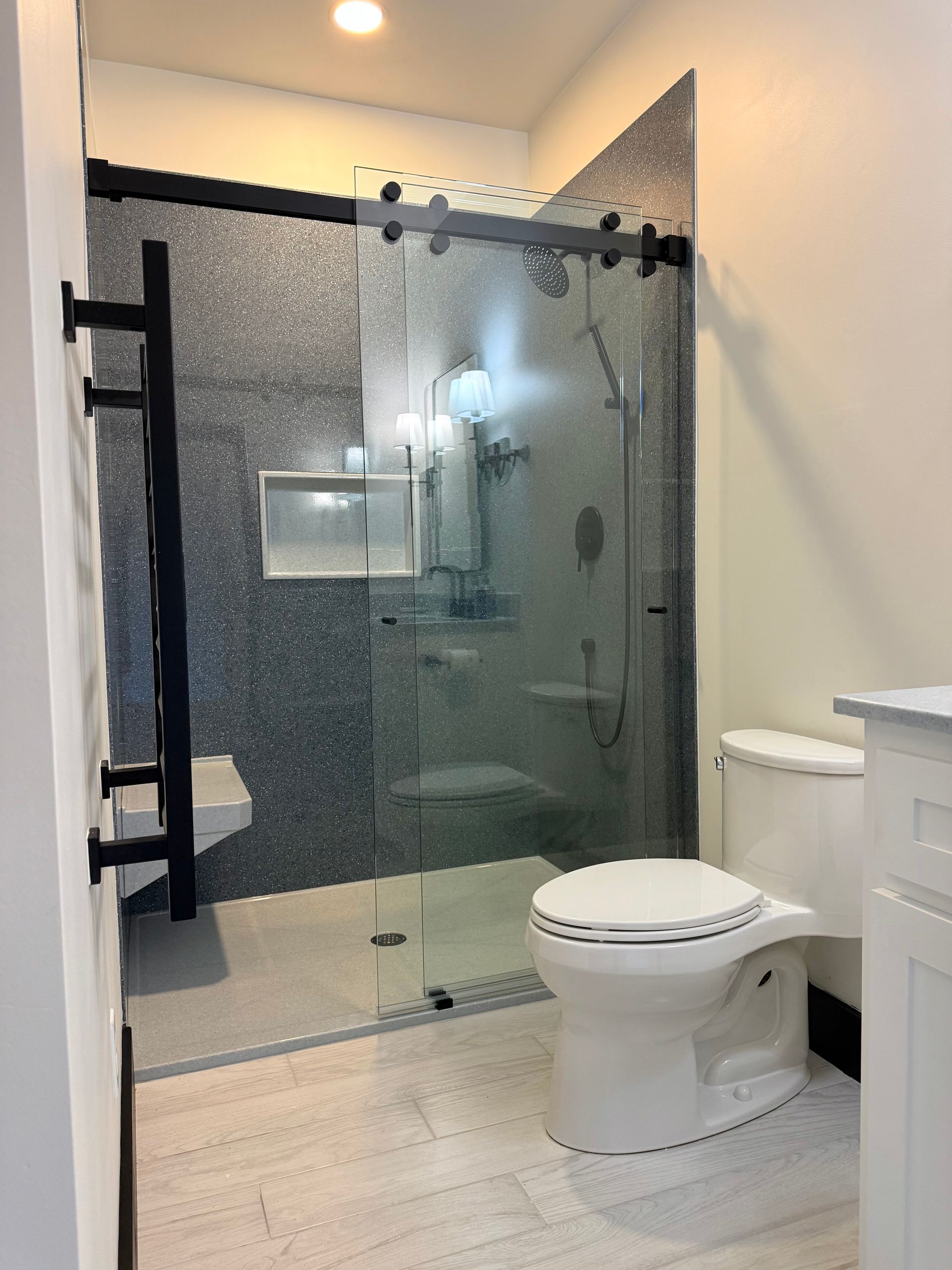 Modern bathroom with glass shower, patterned tile, black fixtures, and white toilet.
