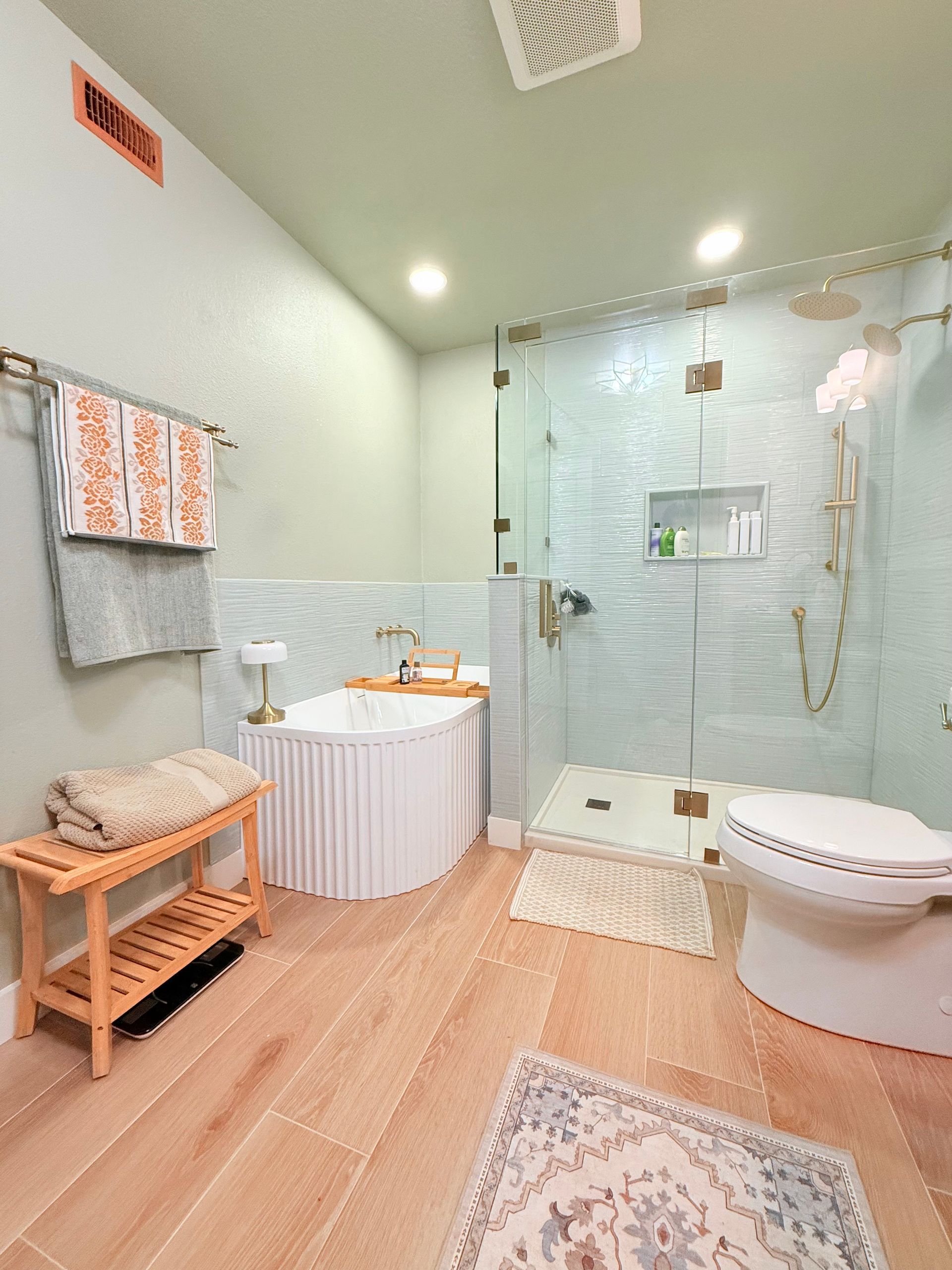 Bathroom with light wood floor, white tub, glass shower, and gold fixtures.