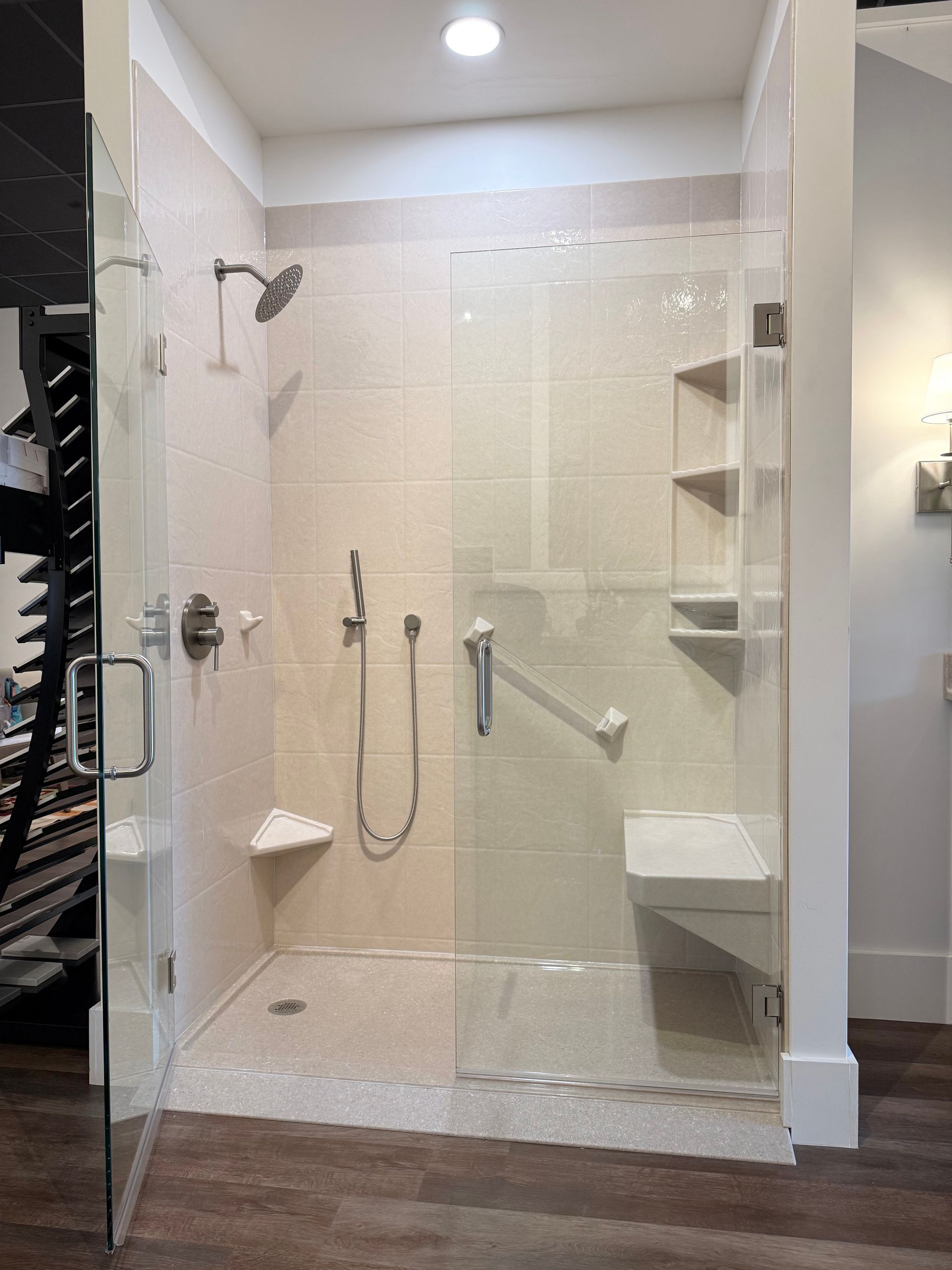 Accessible shower with glass doors, built-in seat, grab bar, and multiple showerheads. Beige tile walls.