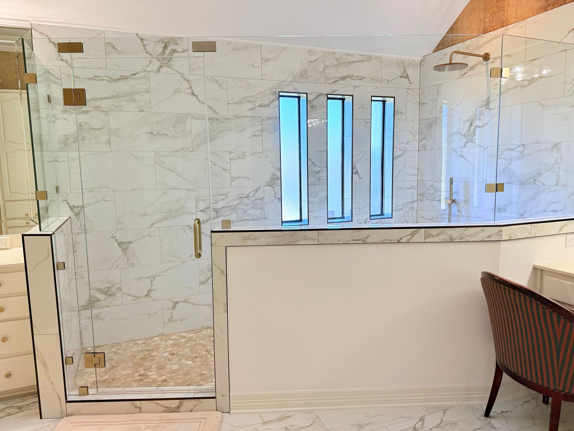 Luxurious shower with marble tile and glass doors, featuring decorative vertical light panels.