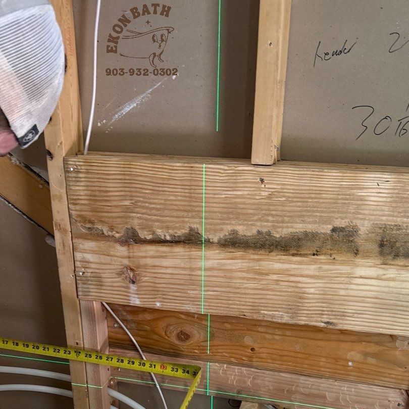 A person is measuring a piece of wood with a tape measure for blocking in a bathroom remodel