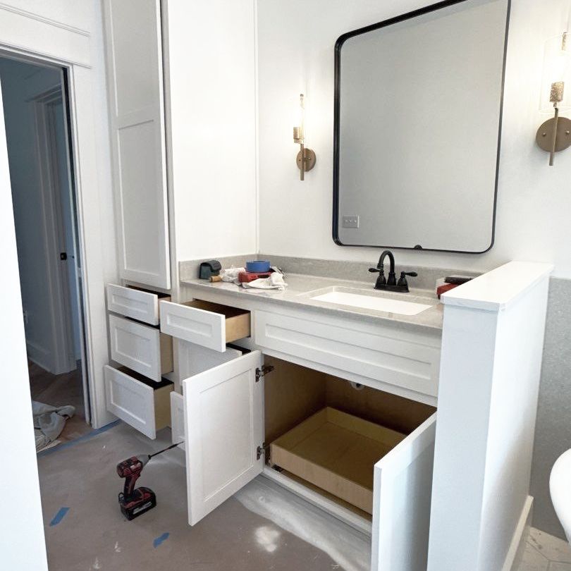 A bathroom with a sink , mirror , cabinets and drawers