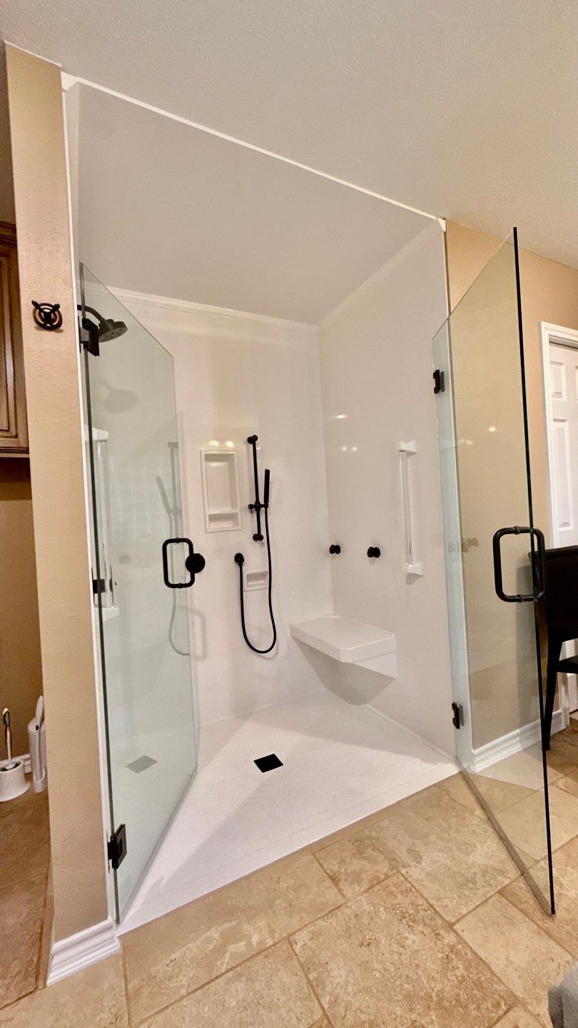 Spacious, white walk-in shower with glass doors, black fixtures, and a built-in seat.