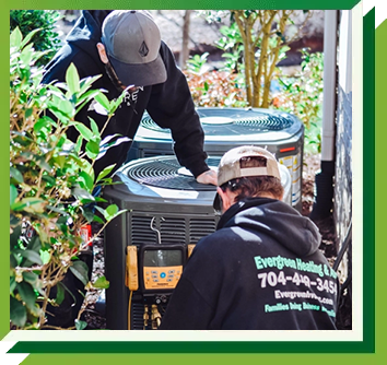 Two technicians in branded hoodies service an outdoor HVAC unit using a digital manifold gauge.
