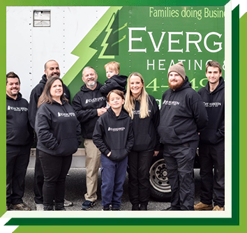 A group of people in branded black hoodies stand in front of a green Evergreen Heating and Cooling service truck.