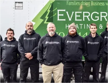 Six people in matching black hoodies stand in front of a green company truck labeled Evergreen Heating & Cooling.