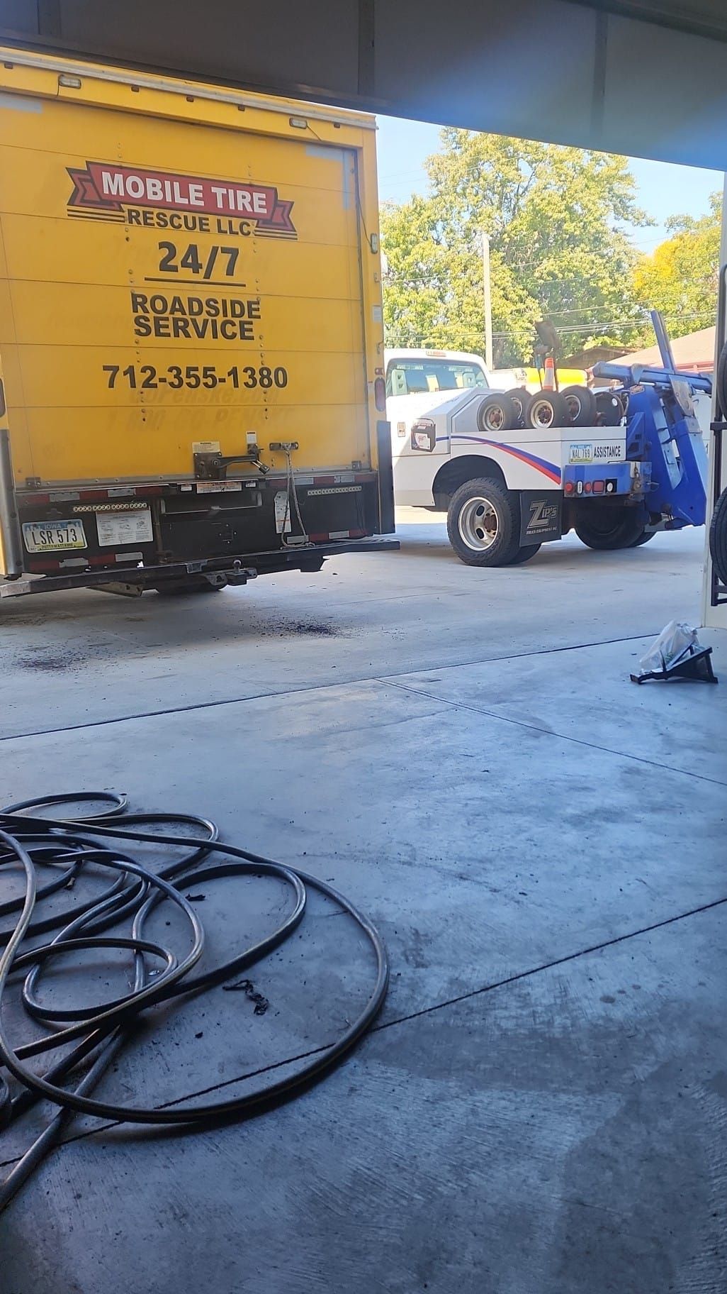 A yellow truck being towed by a tow truck outside a shop. 