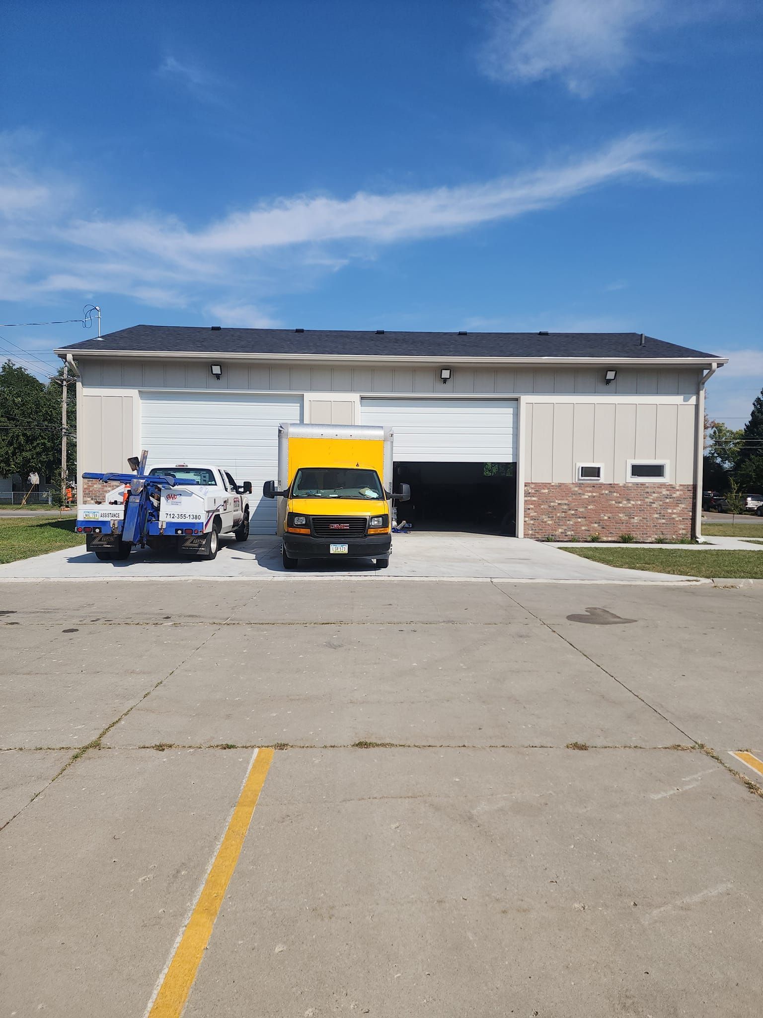 Building with an open garage door, two trucks parked outside, bright blue sky.