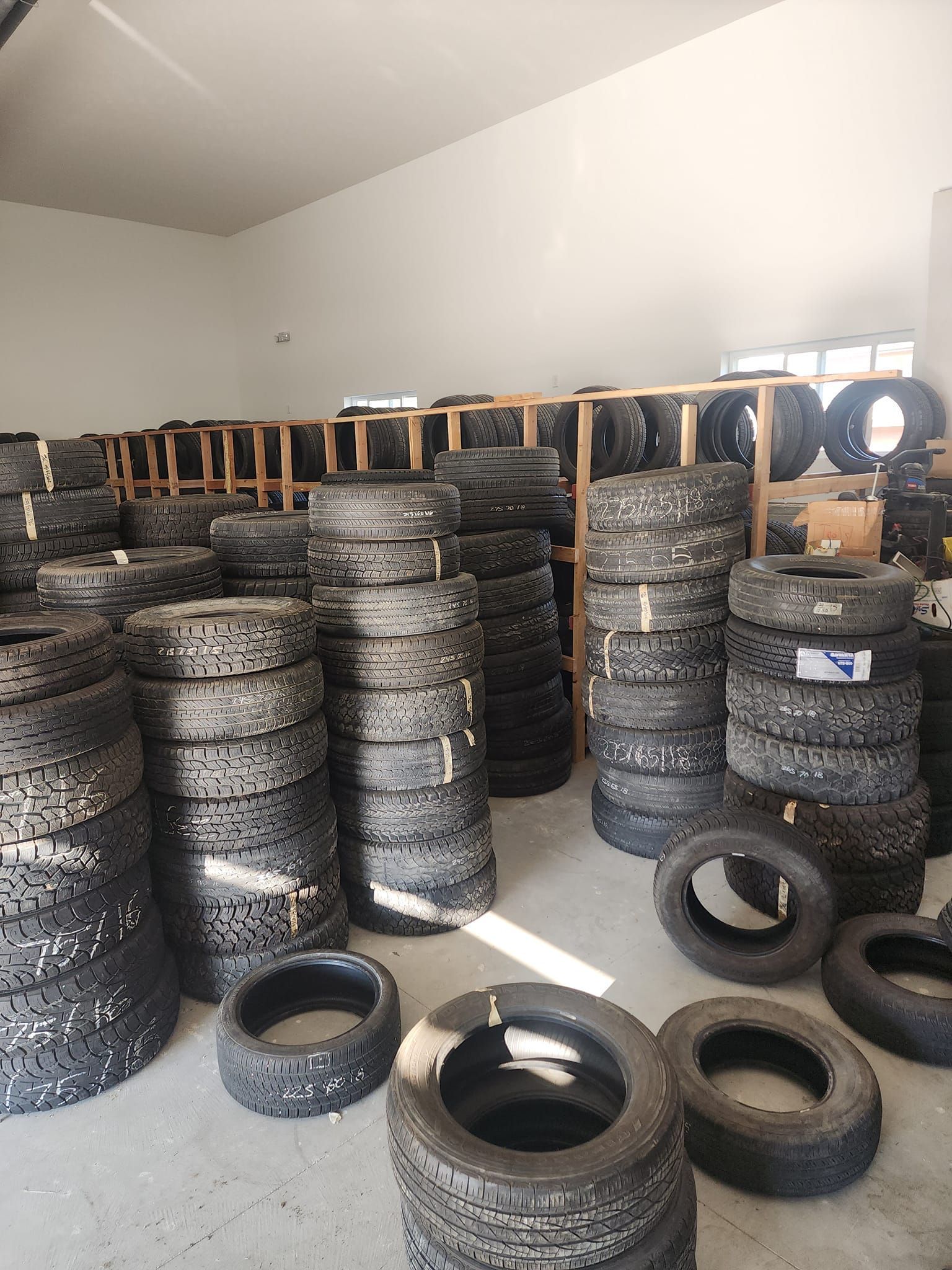 Tires stacked in a warehouse. Many tires of various sizes are visible, on shelves and floor.