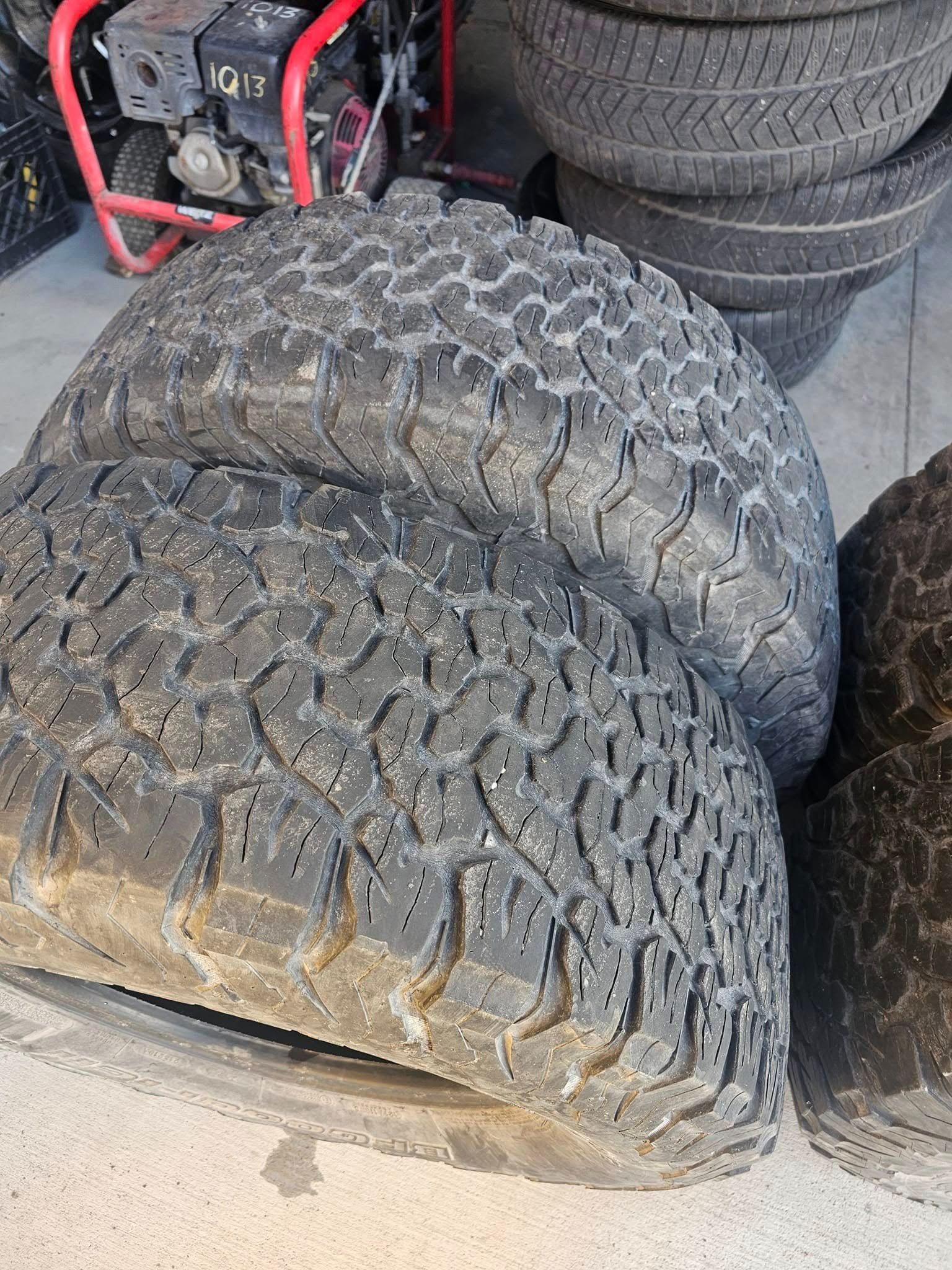 Pile of used off-road tires, with prominent tread patterns, on a concrete surface.