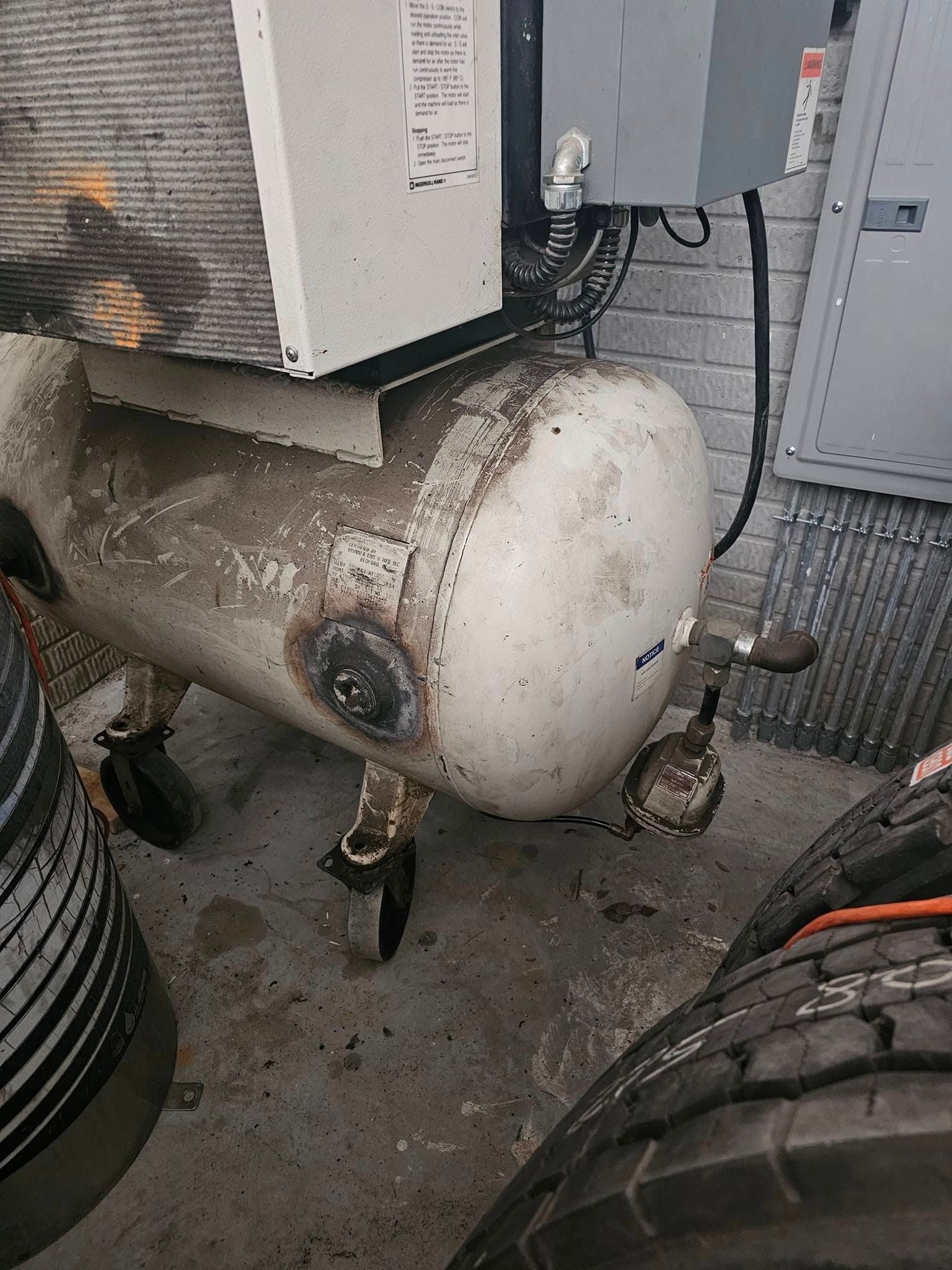White, dirty air compressor on wheels in a garage setting with tires and equipment nearby.