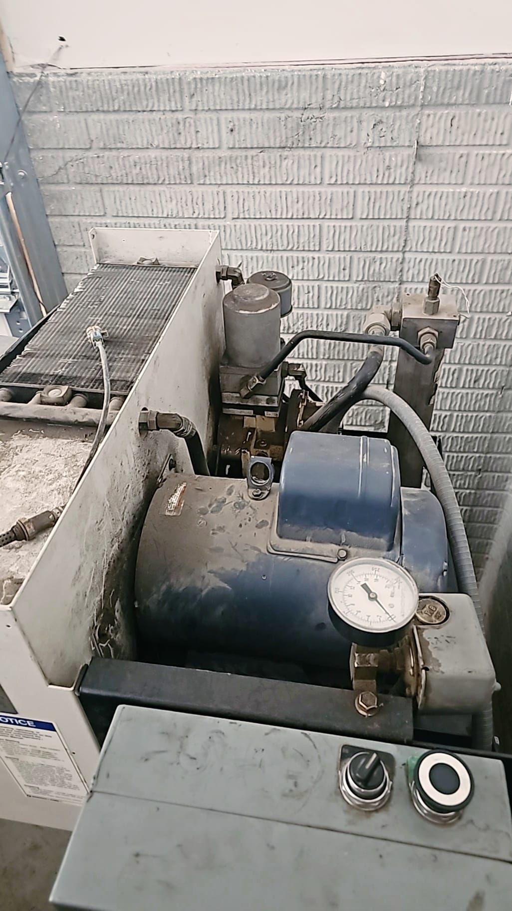 Industrial machine with a blue motor, gauge, and control buttons, against a brick wall.