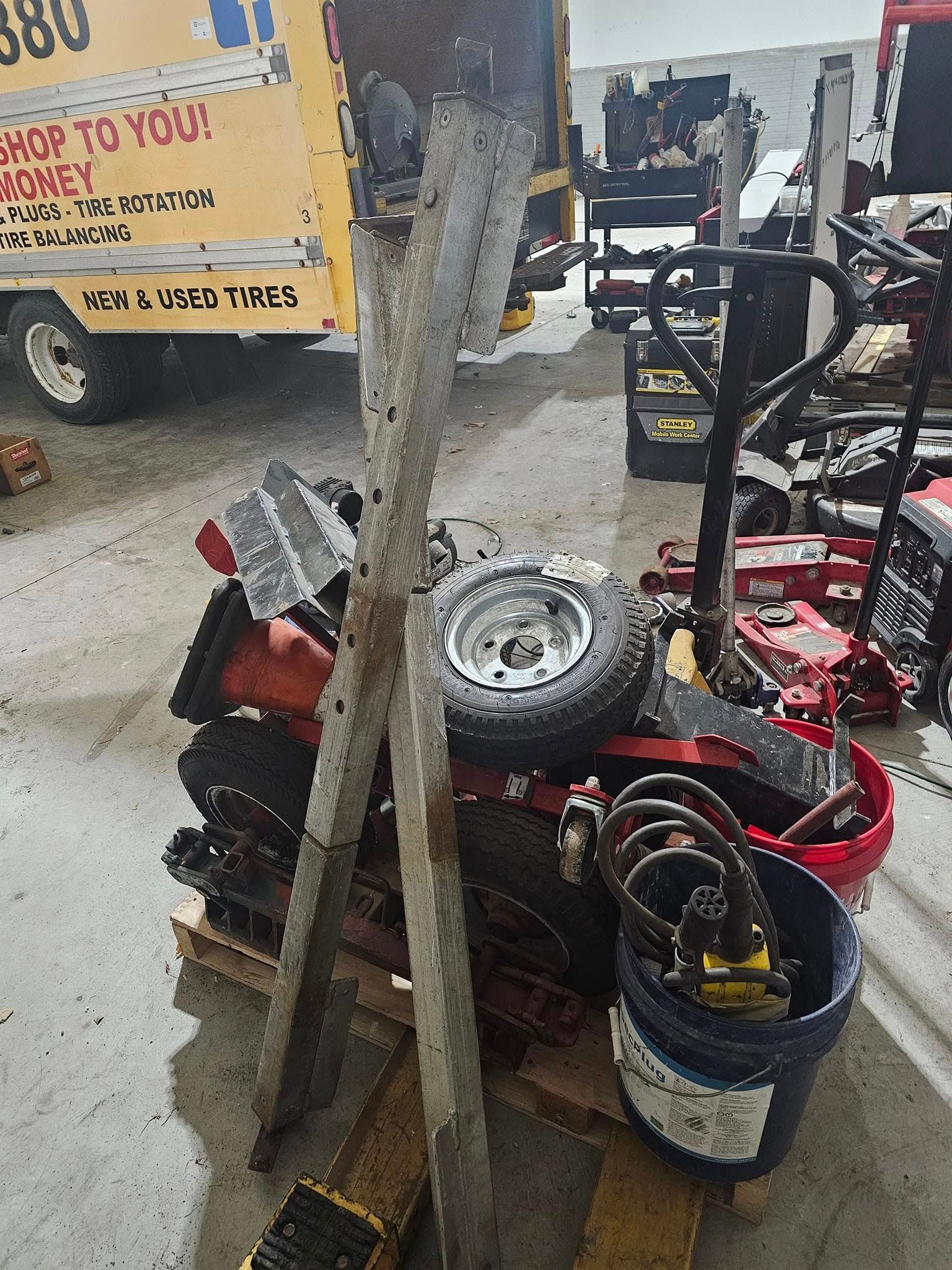 Pile of construction equipment, including a compactor and wheel, in a garage.
