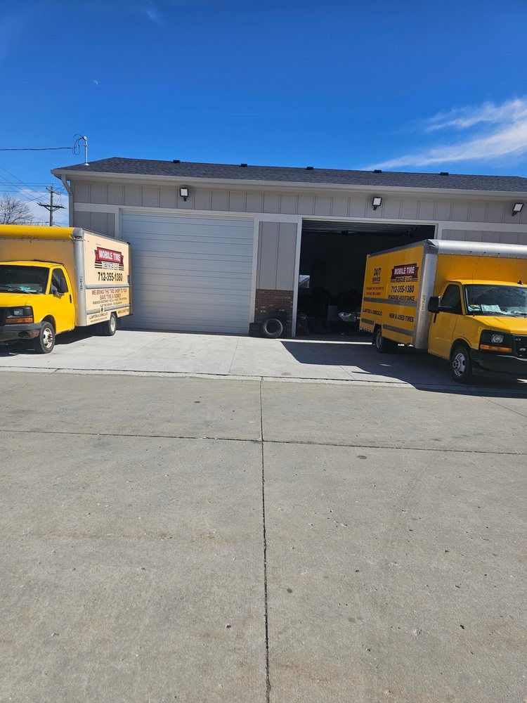 Yellow moving trucks parked in front of a gray garage with the door open on a sunny day.