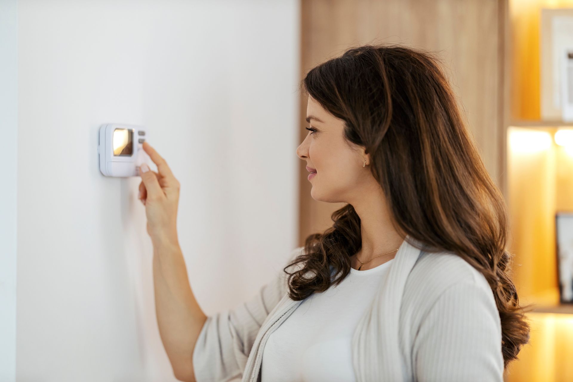 A woman is adjusting a thermostat on a wall.