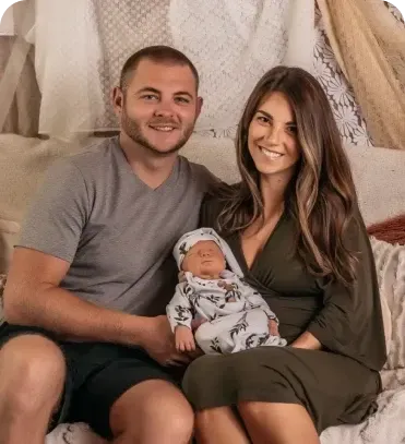 A man and a woman are sitting on a bed with a baby.