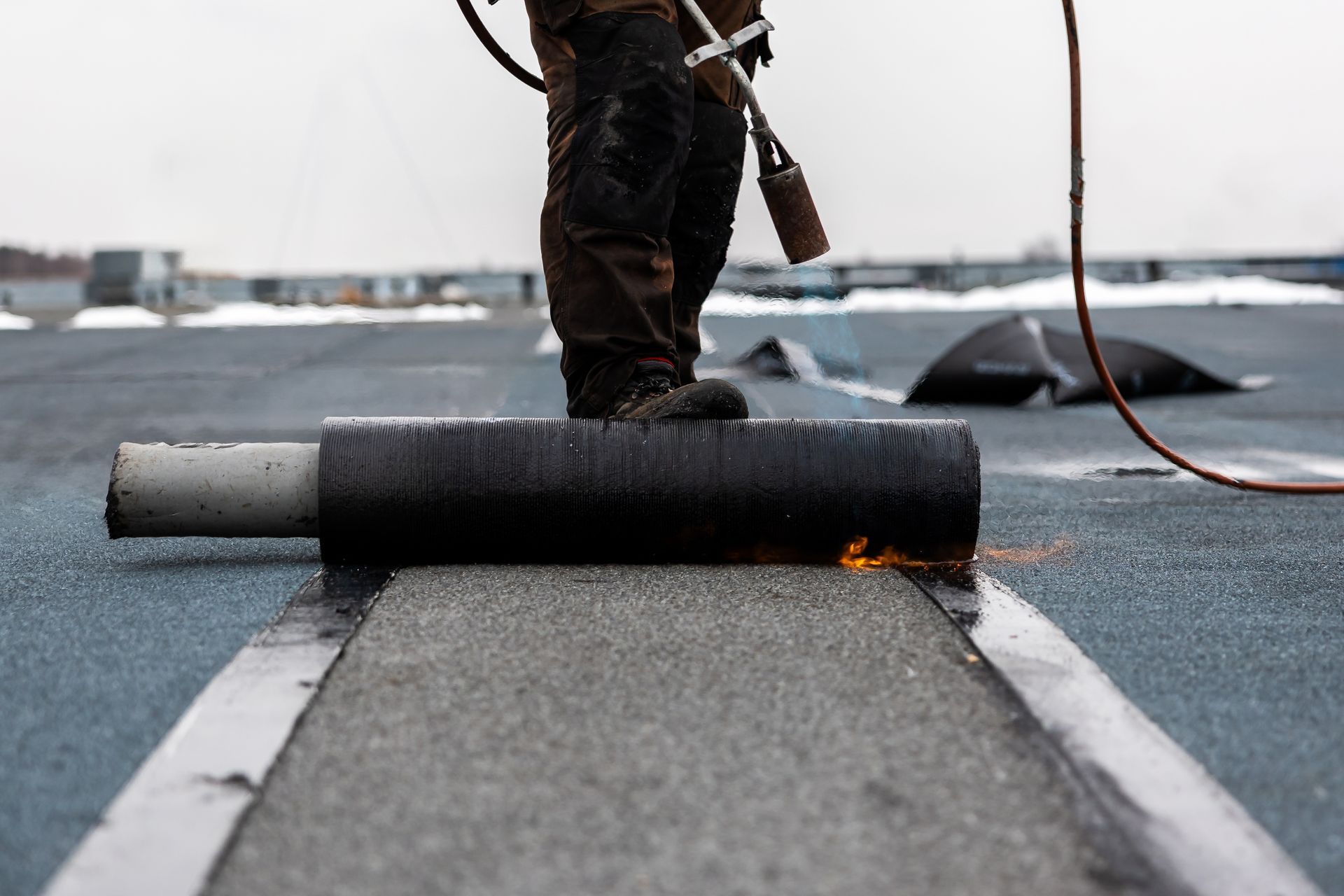 A man is rolling a roll of roofing material on a roof.