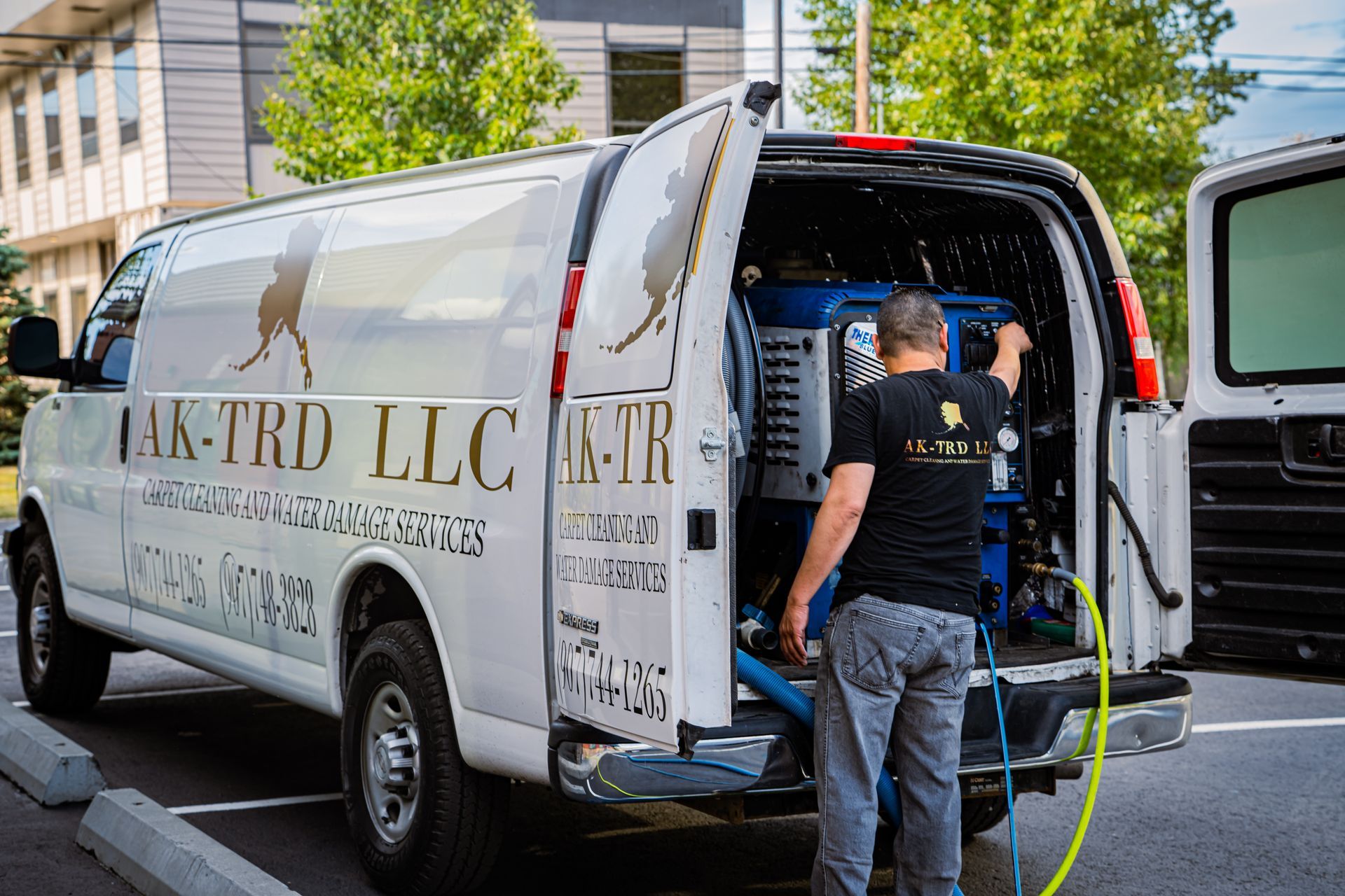 Man using carpet cleaning equipment from a white van; AK-TRD LLC logo on the side.