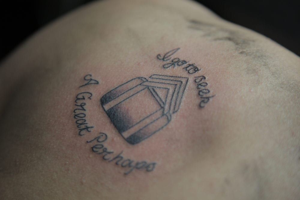 Tattoo on skin, featuring a stack of books within a circle. Text reads 